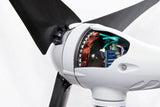Close-up of a white wind turbine blade hub with the inner motor assembly exposed, showing copper windings, green wiring, and electronic components, with part of a black blade visible.