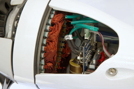 Close-up of a white electric motor showing internal copper windings, green wires, and electronic components through an open side cover.
